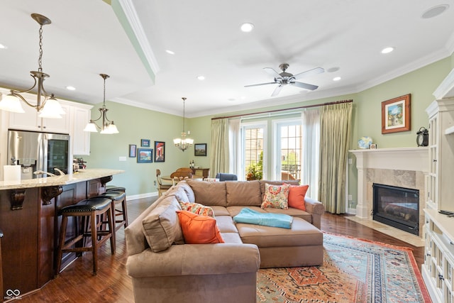 living room featuring crown molding, a premium fireplace, dark hardwood / wood-style flooring, and ceiling fan with notable chandelier