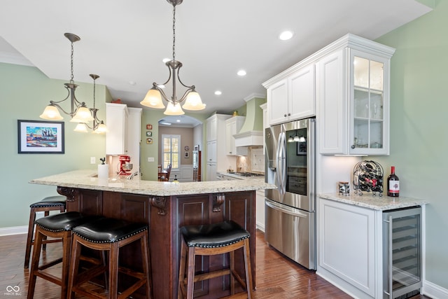 kitchen with a breakfast bar area, premium range hood, white cabinetry, appliances with stainless steel finishes, and beverage cooler