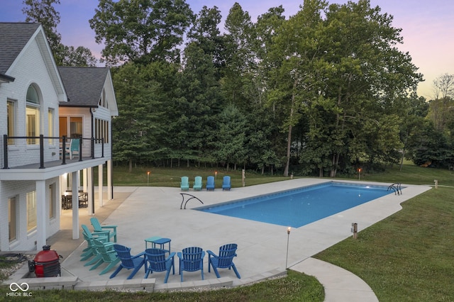 pool at dusk featuring a patio area and a lawn