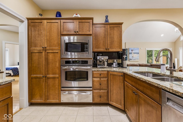 kitchen featuring light tile patterned flooring, sink, decorative backsplash, light stone counters, and stainless steel appliances