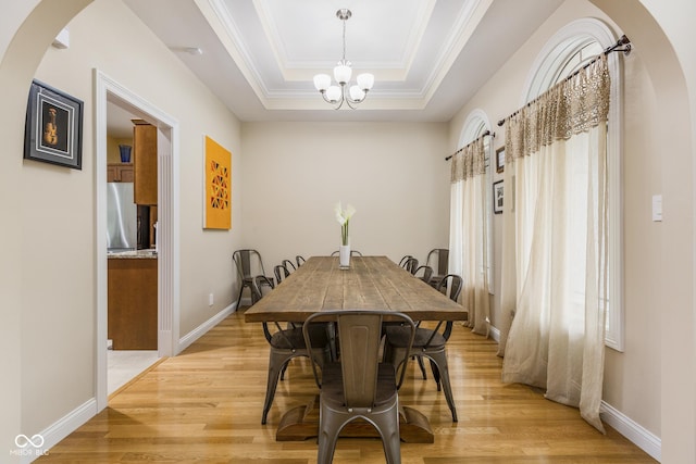 dining space featuring an inviting chandelier, a healthy amount of sunlight, a raised ceiling, and light hardwood / wood-style flooring