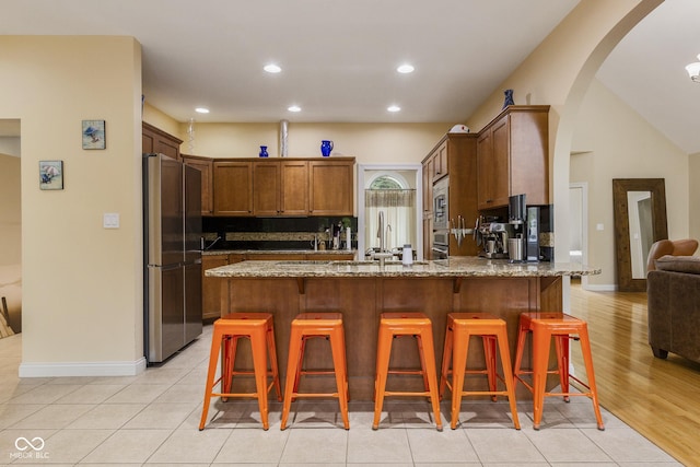 kitchen with light tile patterned floors, a kitchen breakfast bar, stainless steel appliances, light stone countertops, and backsplash