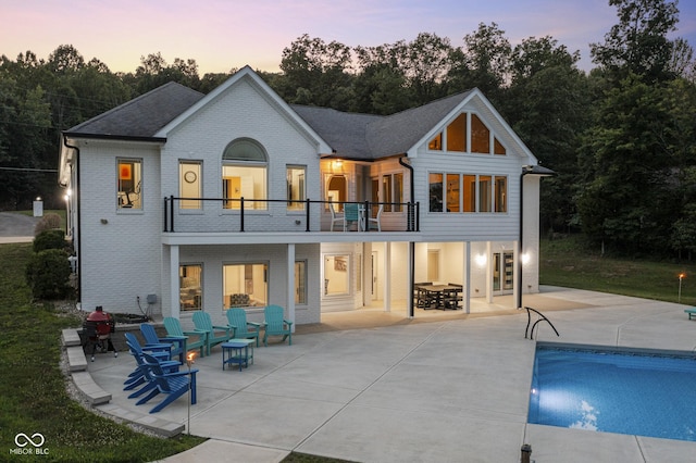 back house at dusk featuring a balcony and a patio