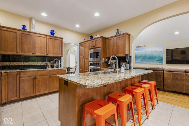 kitchen with a breakfast bar, decorative backsplash, light stone counters, stainless steel appliances, and a center island with sink