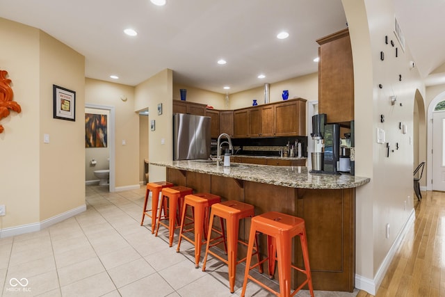 kitchen with sink, a kitchen breakfast bar, stainless steel fridge, kitchen peninsula, and light stone countertops