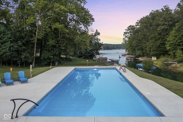 pool at dusk featuring a water view, a yard, and a patio