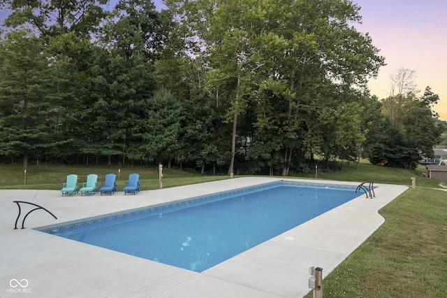 pool at dusk featuring a patio and a lawn