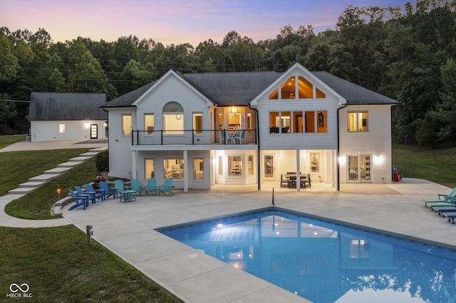 back house at dusk with a patio area, a balcony, and a lawn