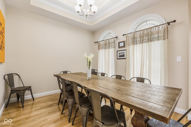 dining room with crown molding, a tray ceiling, a chandelier, and light hardwood / wood-style floors