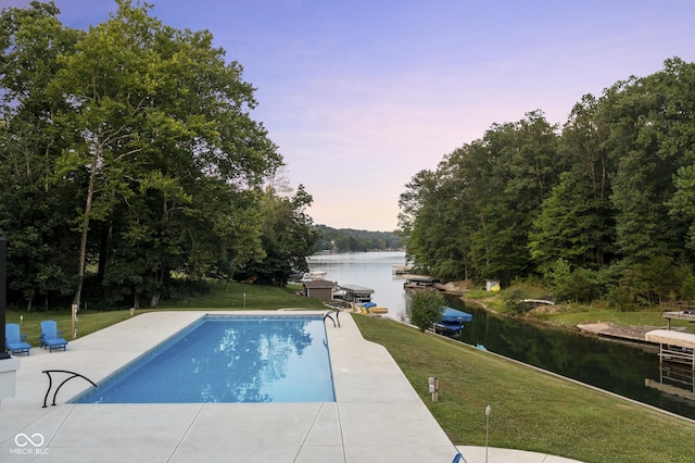 pool at dusk with a water view and a yard