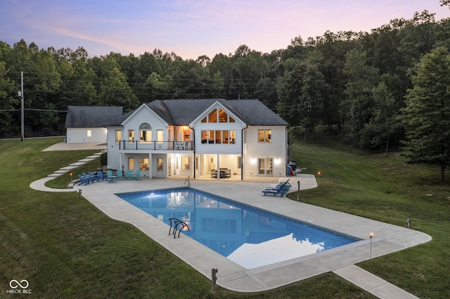 back house at dusk with a patio, a balcony, and a yard