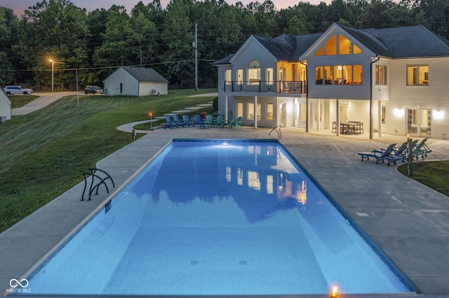 pool at dusk featuring an outbuilding, a patio area, and a lawn