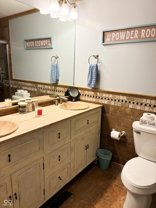 bathroom with toilet, a wainscoted wall, vanity, a shower stall, and tile walls