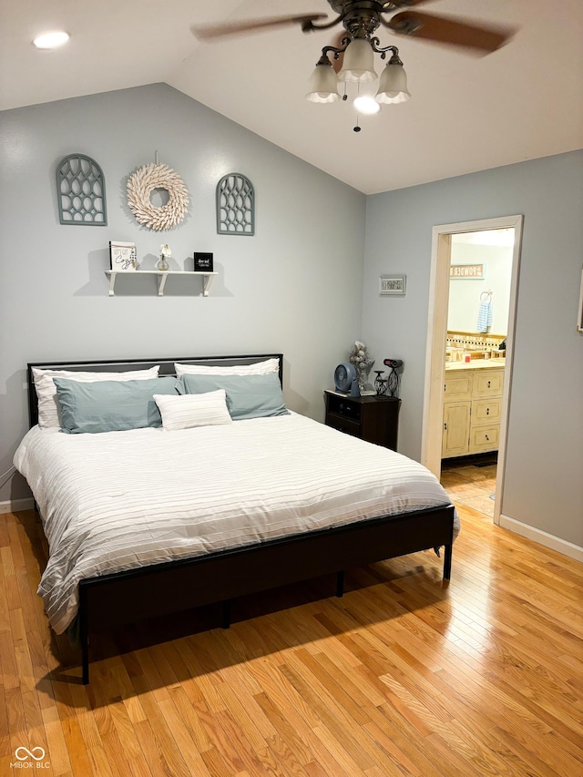 bedroom with ceiling fan, baseboards, vaulted ceiling, light wood-style floors, and ensuite bath