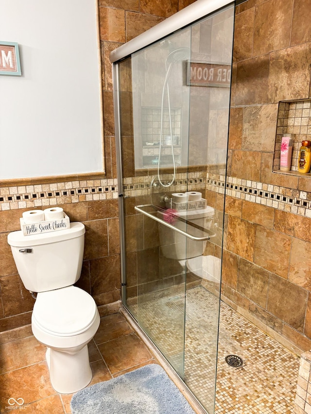 bathroom featuring toilet, a stall shower, tile patterned flooring, and tile walls