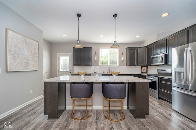 kitchen featuring wood-type flooring, hanging light fixtures, a center island, and stainless steel appliances