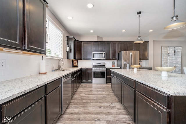 kitchen with appliances with stainless steel finishes, decorative backsplash, sink, light wood-type flooring, and pendant lighting