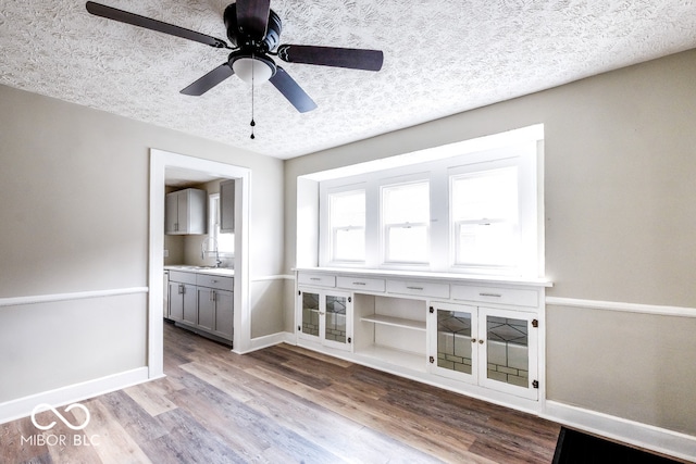 unfurnished living room featuring light hardwood / wood-style flooring, a textured ceiling, sink, and ceiling fan