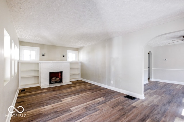 unfurnished living room with ceiling fan, a fireplace, a textured ceiling, and dark hardwood / wood-style floors