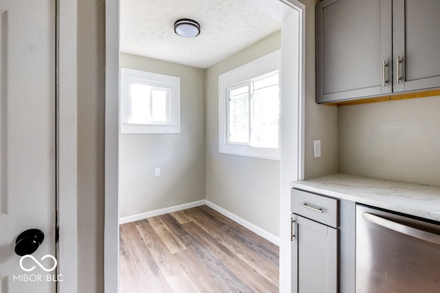 kitchen with gray cabinetry, light stone countertops, light hardwood / wood-style flooring, and stainless steel dishwasher