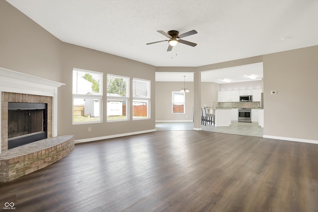 unfurnished living room with ceiling fan, wood-type flooring, a brick fireplace, and a textured ceiling