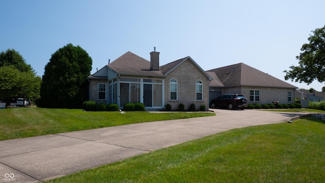 ranch-style house with brick siding, a sunroom, driveway, a front lawn, and a chimney