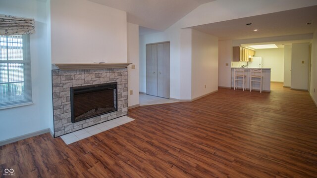 unfurnished living room with vaulted ceiling, a stone fireplace, and hardwood / wood-style floors