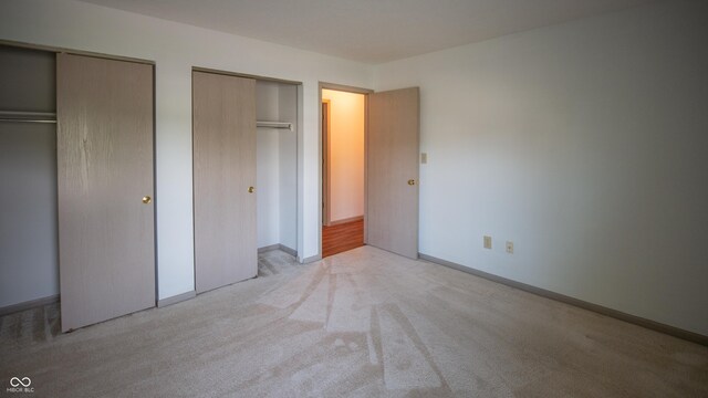 unfurnished bedroom with two closets and light carpet