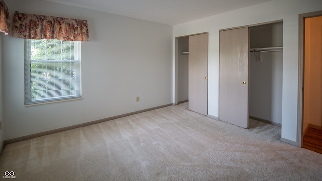 unfurnished bedroom featuring multiple closets and light carpet