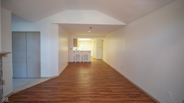 corridor featuring vaulted ceiling, baseboards, and wood finished floors