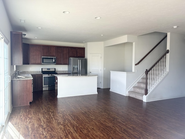 kitchen with sink, appliances with stainless steel finishes, dark hardwood / wood-style flooring, a kitchen island, and light stone countertops