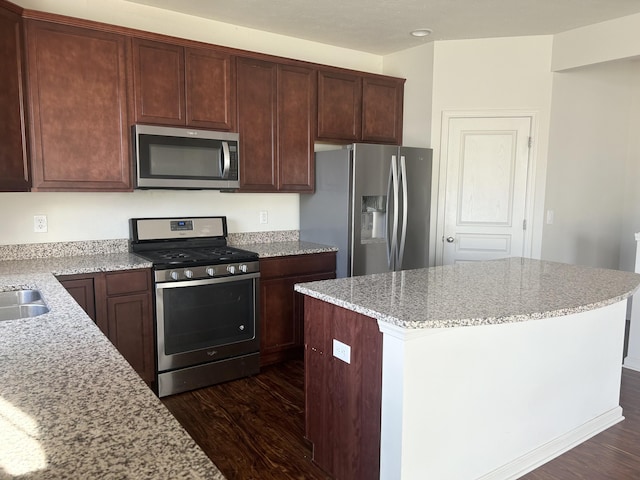 kitchen with appliances with stainless steel finishes, dark hardwood / wood-style floors, sink, a center island, and light stone countertops