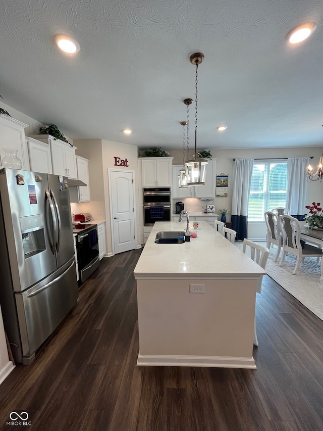 kitchen with appliances with stainless steel finishes, pendant lighting, dark hardwood / wood-style floors, and an island with sink