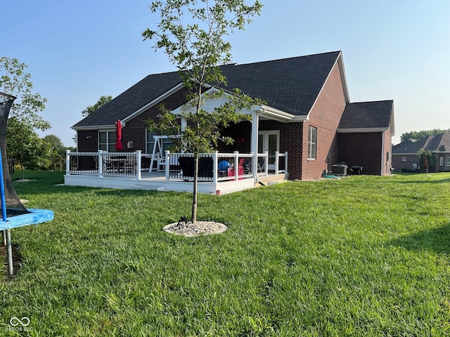 back of house featuring a yard, a deck, a trampoline, and a patio area