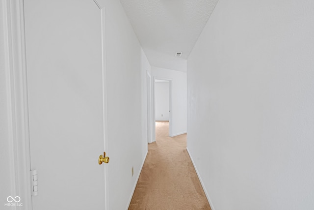 corridor with light carpet and a textured ceiling