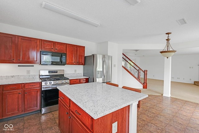 kitchen with appliances with stainless steel finishes, hanging light fixtures, a center island, light stone countertops, and a textured ceiling