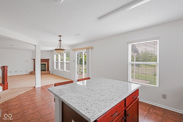 kitchen featuring a kitchen island, a fireplace, decorative light fixtures, light stone countertops, and a textured ceiling