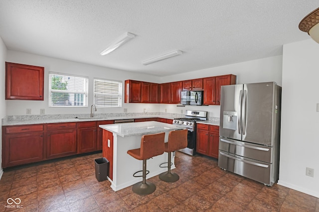 kitchen with sink, a breakfast bar area, a textured ceiling, appliances with stainless steel finishes, and a kitchen island