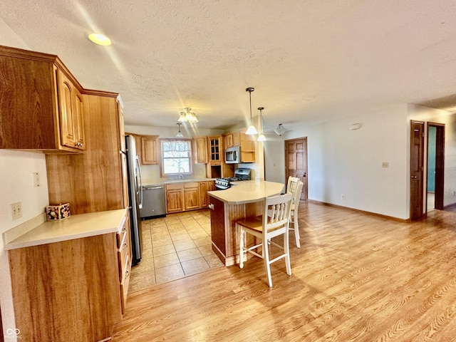 kitchen with stainless steel appliances, a breakfast bar, brown cabinetry, and light countertops