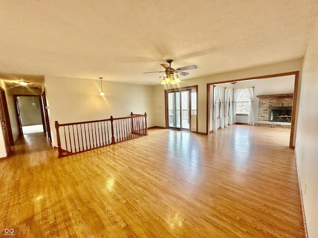 spare room with a textured ceiling, a fireplace, a ceiling fan, and light wood-style floors