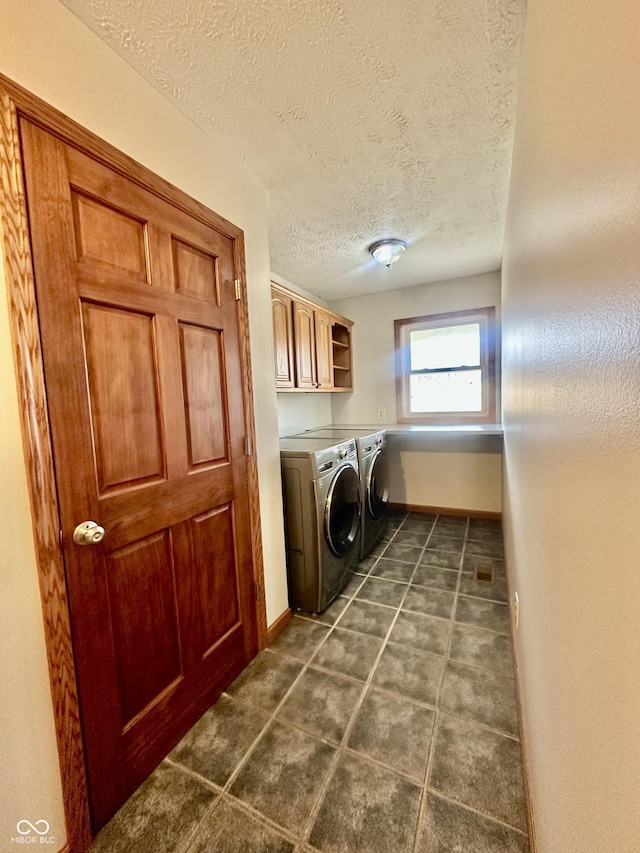 clothes washing area featuring cabinet space, washing machine and dryer, a textured ceiling, dark tile patterned floors, and baseboards