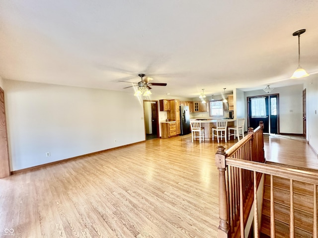 unfurnished living room featuring ceiling fan, light wood-type flooring, and baseboards