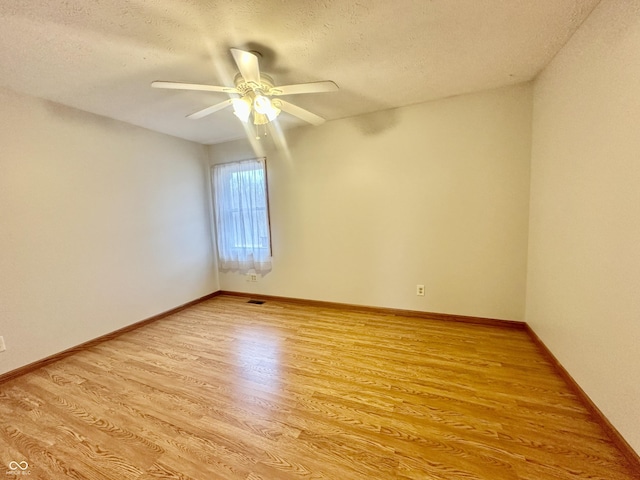 empty room with a textured ceiling, visible vents, baseboards, a ceiling fan, and light wood-style floors