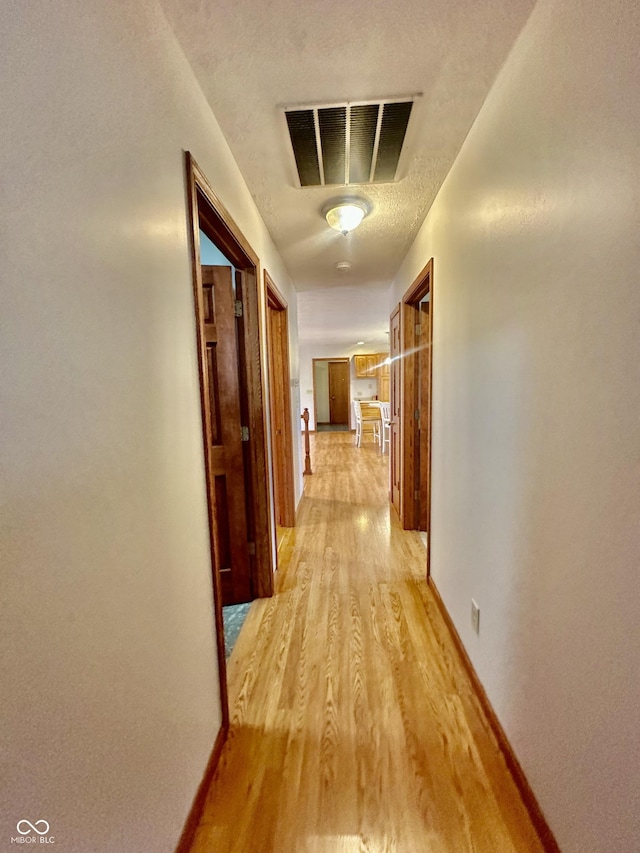 hall featuring light wood-type flooring, baseboards, visible vents, and a textured ceiling