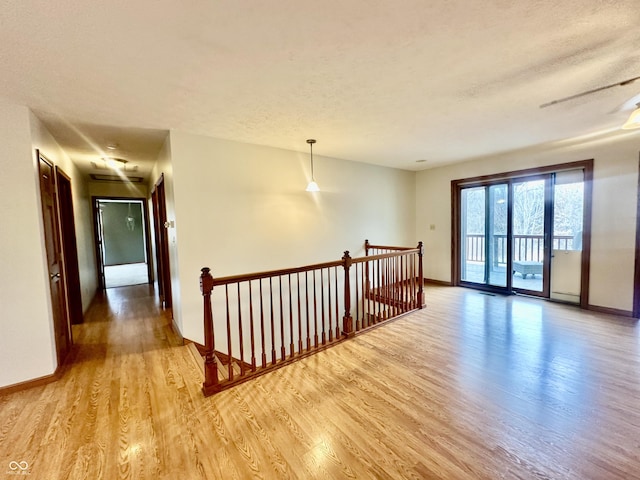 unfurnished room with light wood-type flooring, baseboards, and a textured ceiling