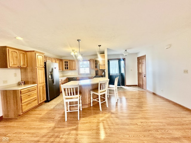 kitchen with a breakfast bar area, light countertops, light wood-style flooring, glass insert cabinets, and stainless steel fridge