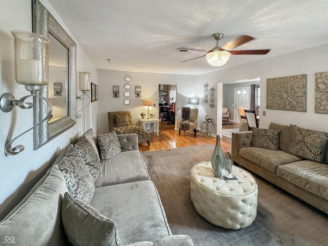 living room with a textured ceiling, ceiling fan, and light hardwood / wood-style floors