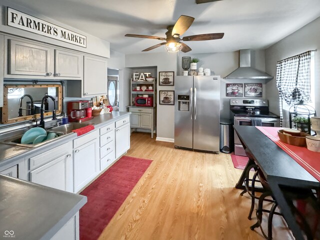 kitchen with light wood-type flooring, white cabinets, ceiling fan, stainless steel appliances, and wall chimney exhaust hood