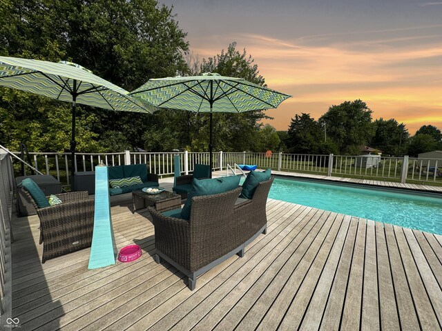 pool at dusk featuring a wooden deck and an outdoor hangout area