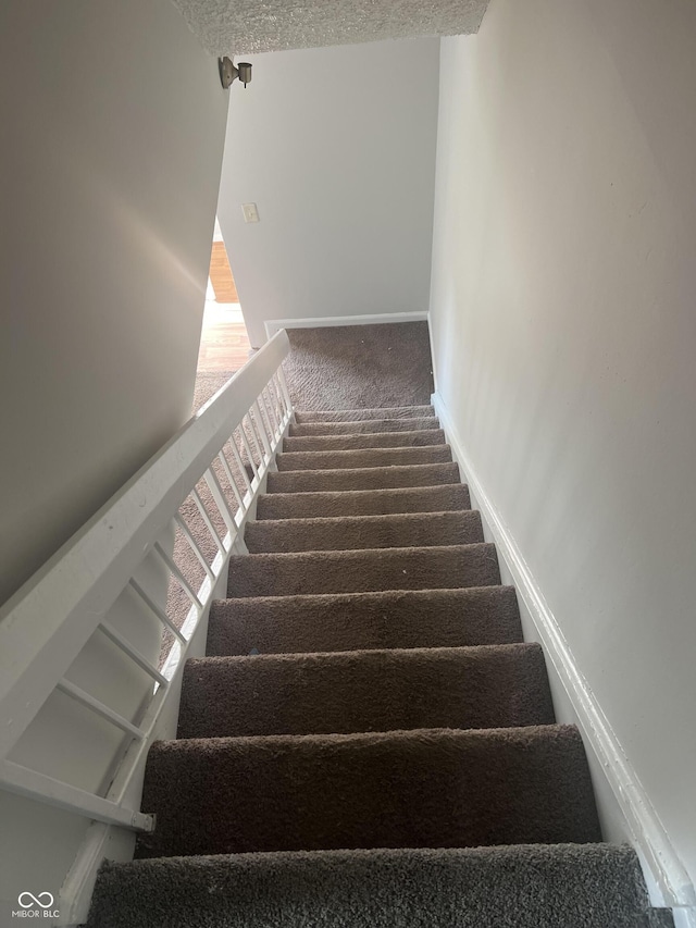 stairway with carpet flooring and a textured ceiling